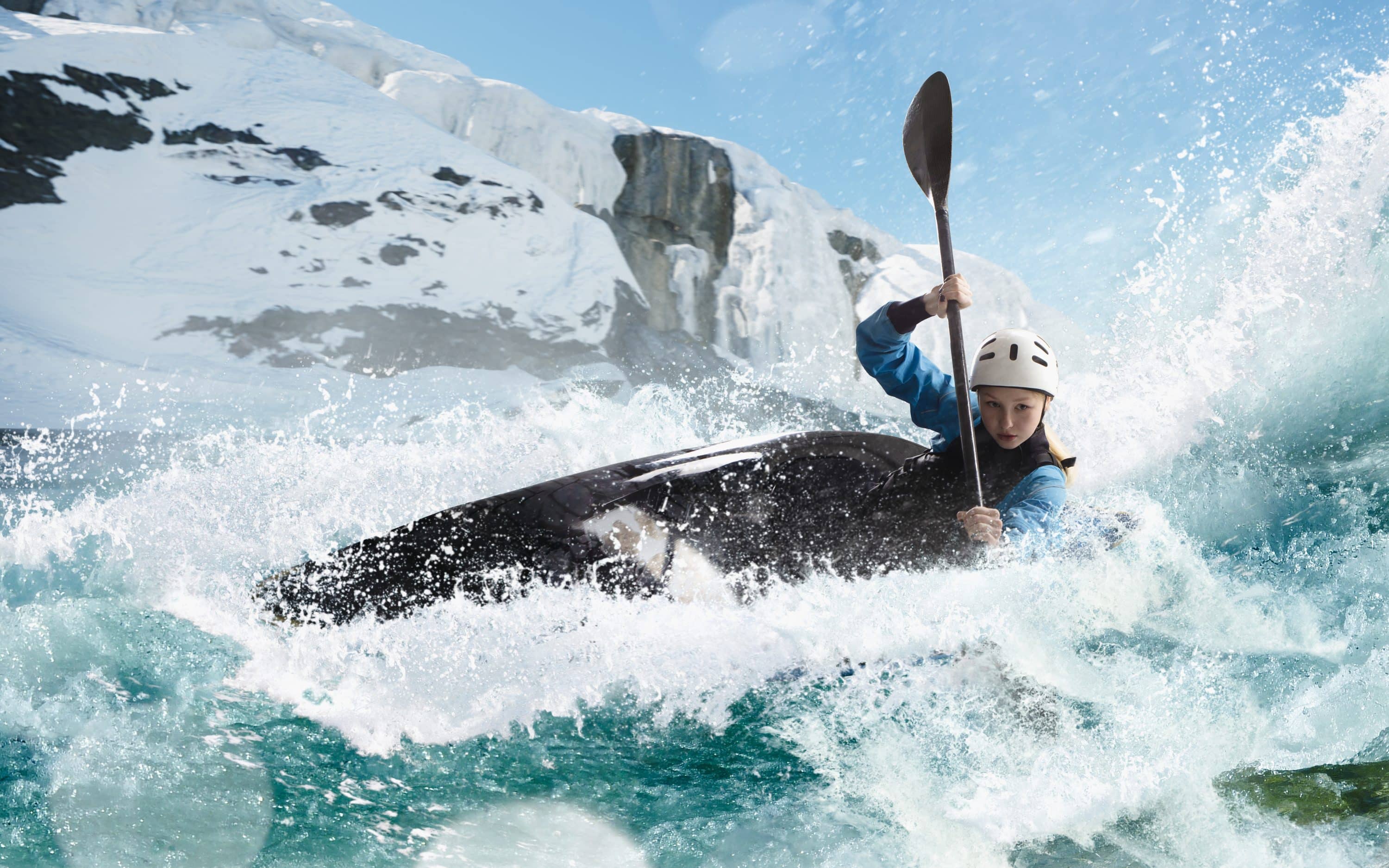 Woman rides a kayak over river rapids